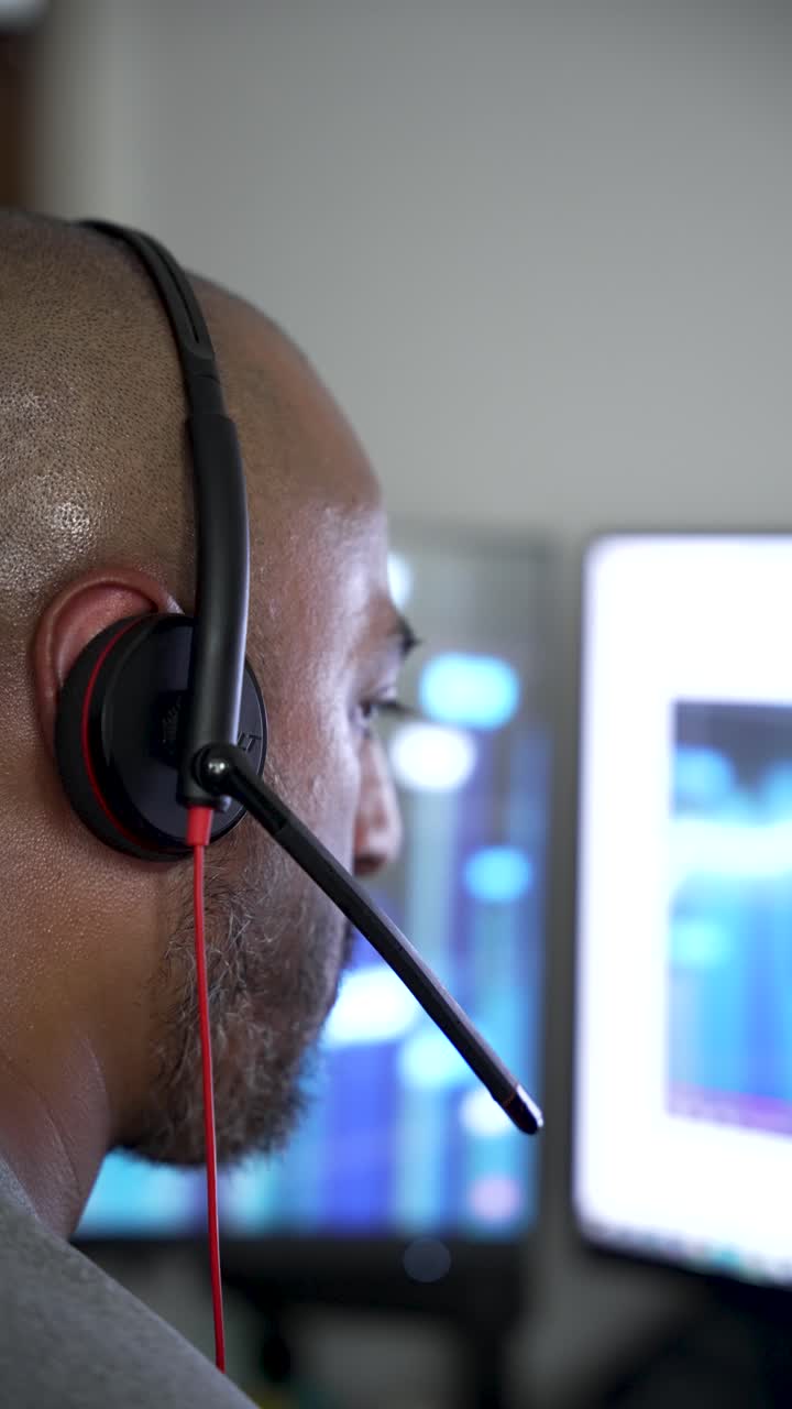 South asian male operator concentrating on computer screen while wearing headset in modern office. vertical video
