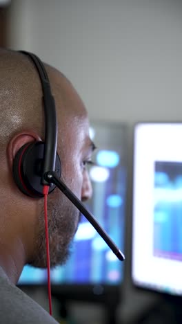 south asian male operator concentrating on computer screen while wearing headset in modern office. vertical video