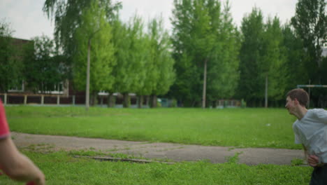 a father throws a soccer ball to his son, who skillfully heads it away in a grassy field with a blurred view of a paved road and greenery in the background