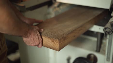 man pushes large plank into a stationary planer