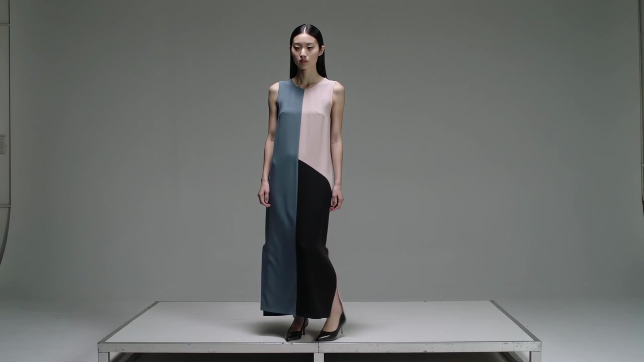 Stepping onto raised platform, Asian model walking and presenting color-block maxi dress in studio