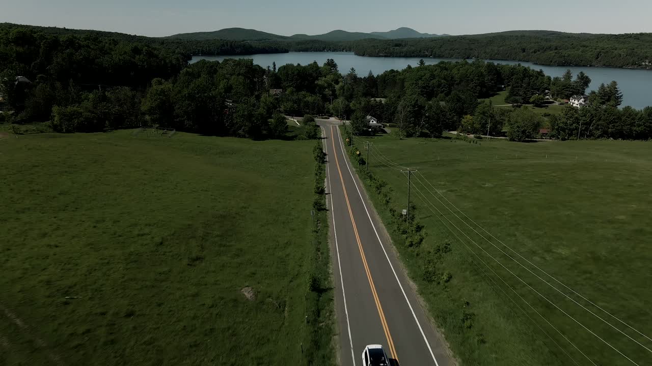 밝은 날씨에 캐나다 퀘벡의 아스팔트 도로를 달리는 흰색 자동차 - 오름차순 드론 샷