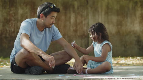 feliz padre asiático y su pequeña hija dibujando con tizas