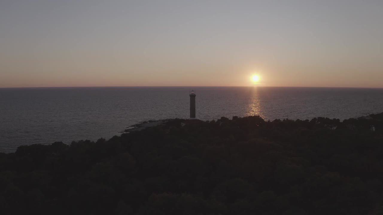 Naturskøn luftfoto af et kystfyrtårn på Dugi Otok, Kroatien, oplyst bagfra af den nedgående sol og omgivet af åbent hav