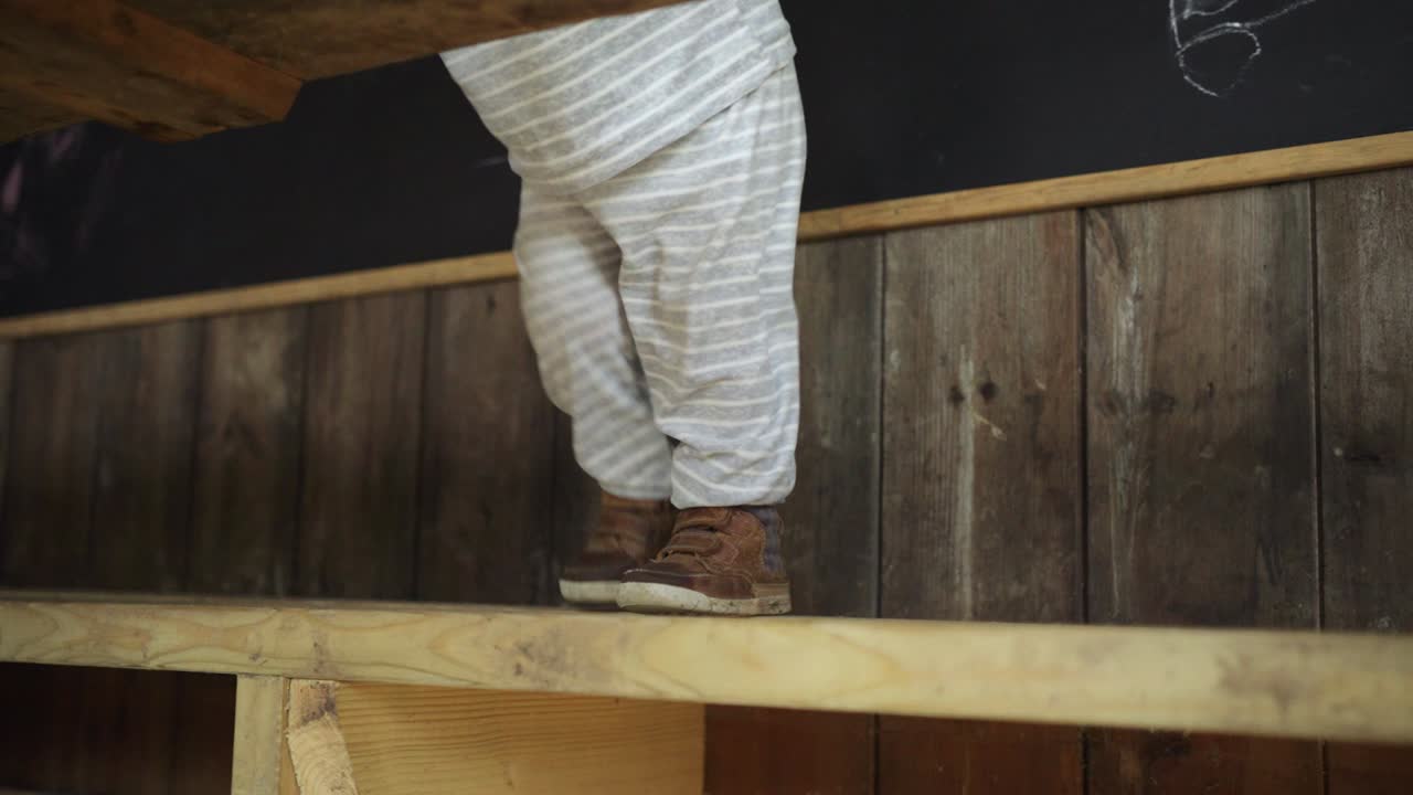 어린 소년은 나무 벤치에 서서 오두막에 있는 나무 테이블에 몸을 기댄다
