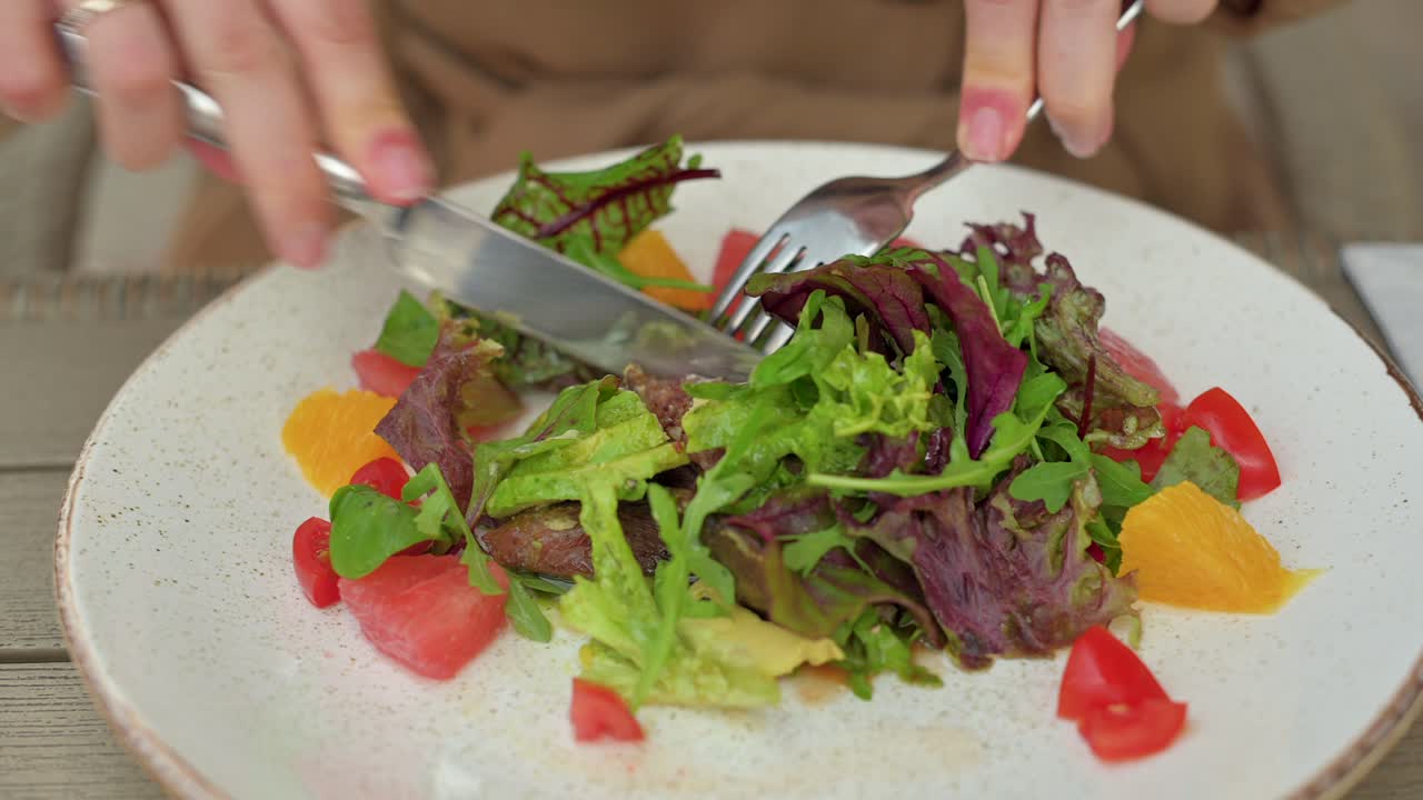 Woman in brown coat eating a salad at a terrace