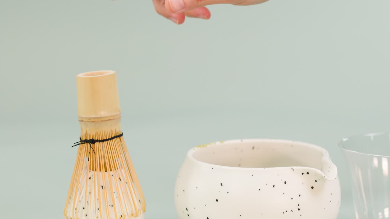 Hand uses bamboo whisk to mix matcha tea in ceramic bowl, soft lighting, static camera