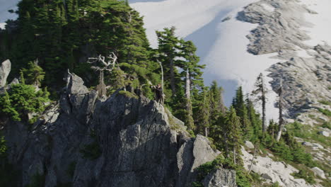 Photographer-prepares-for-epic-shot-with-camera-on-mountain-ridge,-Tim-Durkan-wide-tracking-helicopter-counterclockwise-orbit-pull-back-SLOW-MOTION