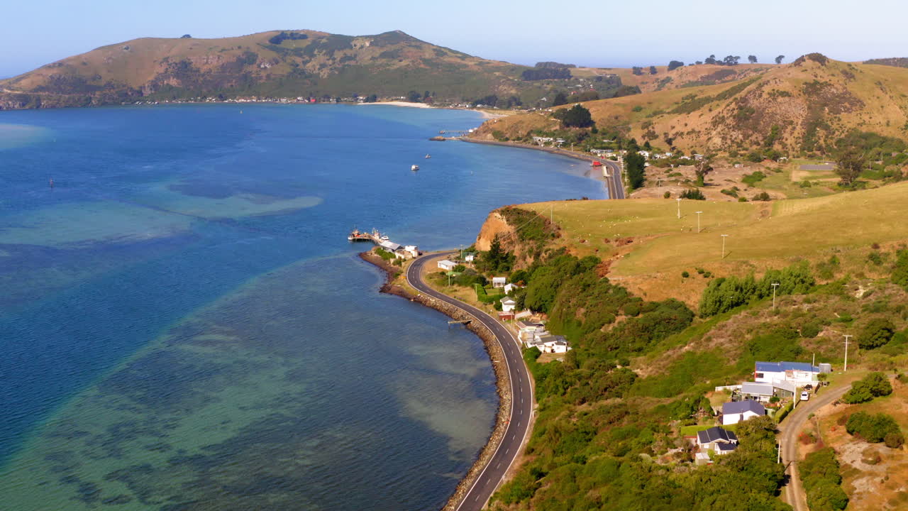 Aerial View of a Scenic Coastal Road Winding Along a Clear Bay with Houses