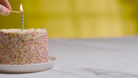 Studio-Shot-Birthday-Cake-Covered-With-Decorations-And-Single-Candle-Being-Lit-2