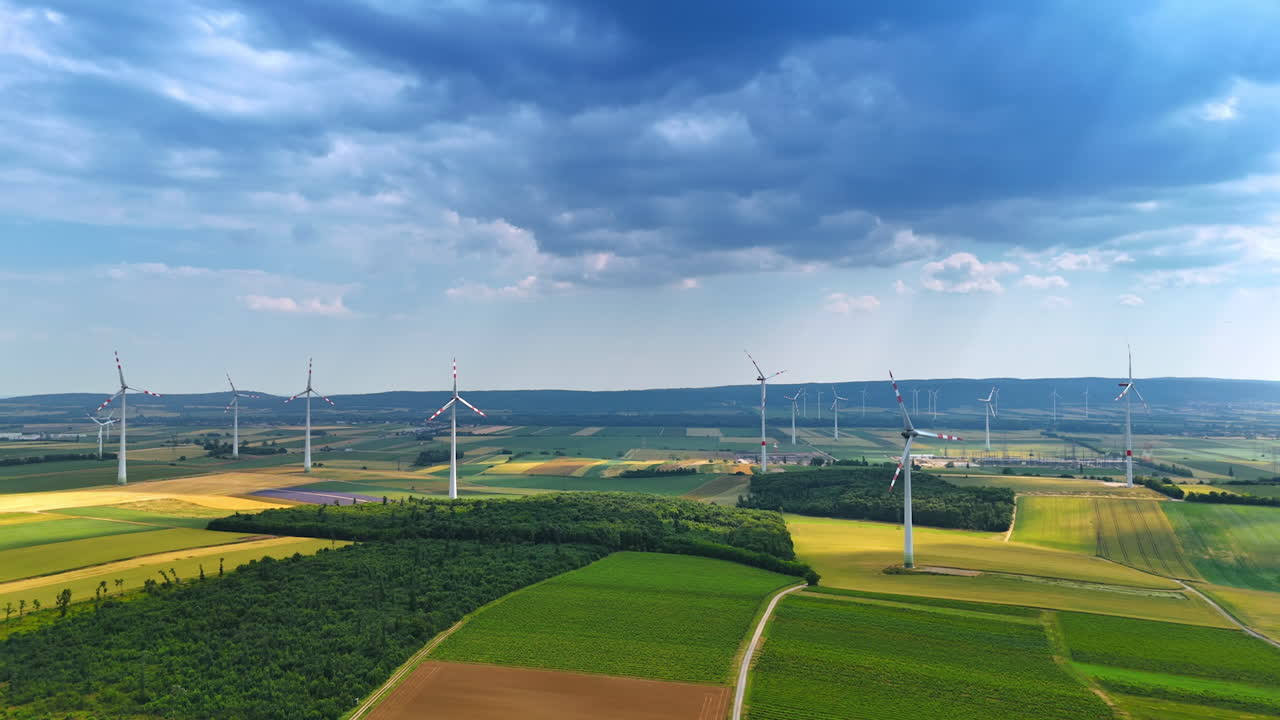 Dramatic cloudscape covering the sky over the vast fields with wind turbines. Aerial perspective on the countryside used for green energy production