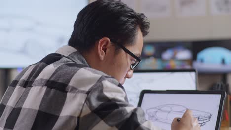 vista lateral de cerca de un hombre asiático dibujando un nuevo concepto de diseño de automóvil en una tableta en el estudio con televisión y computadoras muestra modelo de automóvil eléctrico 3d