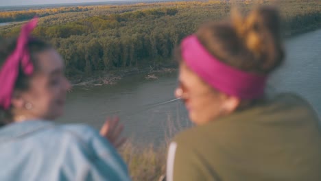 girls-look-at-sailing-motorboat-from-steep-bank-in-evening