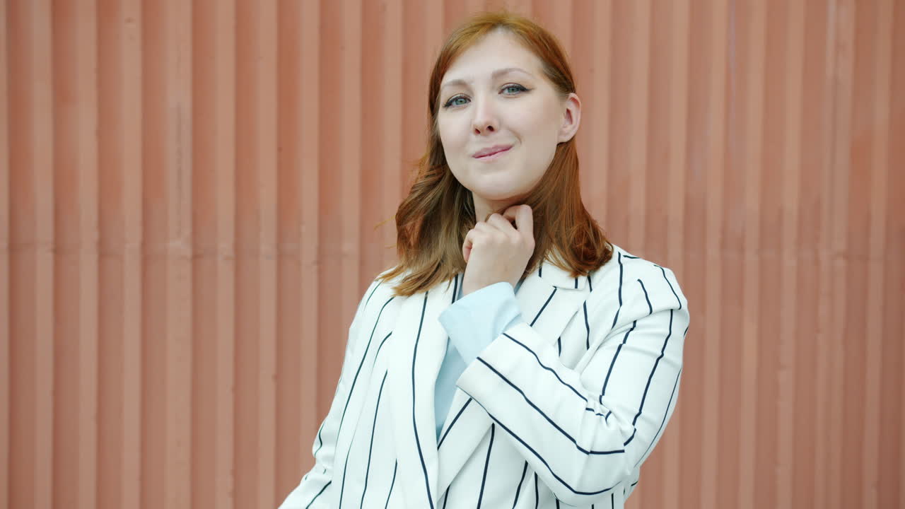 Woman in striped blazer, smiling, and giving an ok sign in front of a corrugated metal wall