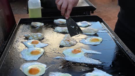 Closeup-of-many-fried-eggs-being-flipped-and-cooked-on-a-hot-oily-griddle-plate-on-an-Australian-barbecue