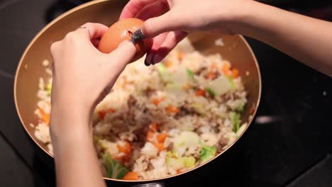 cracking eggs into a wok of fried rice