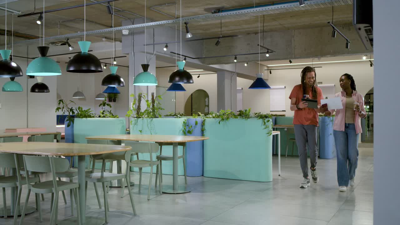 Compañeros de trabajo afroamericanos caminando en la oficina después de revisar una tablet y papel, sosteniendo una taza para revisar.
