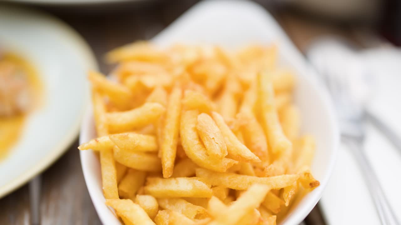 En hand tar gyllene pommes frites från en skål på ett träbord i naturligt dagsljus, närbild