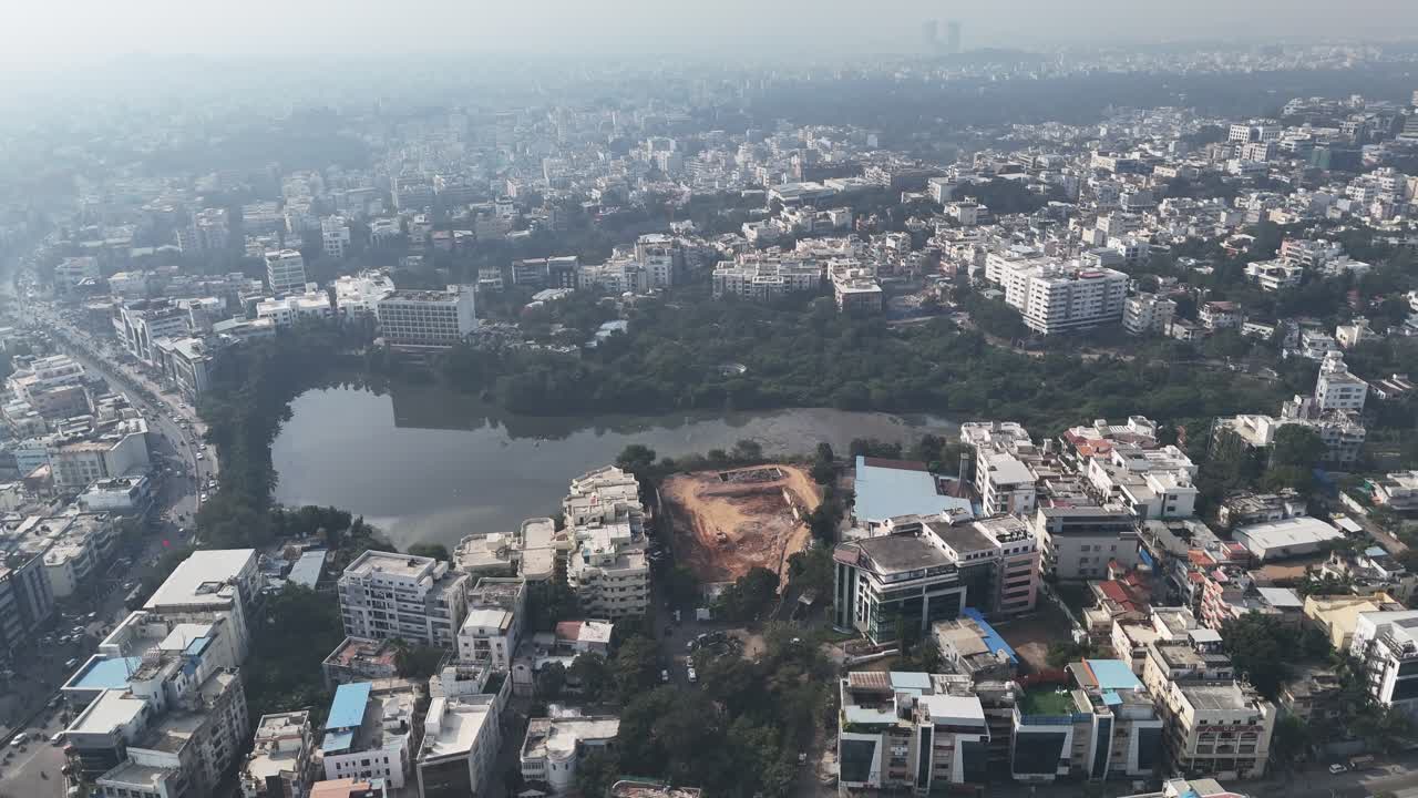 Vista aerea di Hyderabad con un piccolo lago urbano, verde circostante e densi edifici residenziali sotto una leggera foschia diurna.