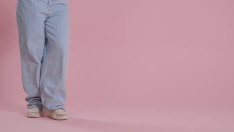 close up on legs and feet of woman having fun dancing against pink studio background