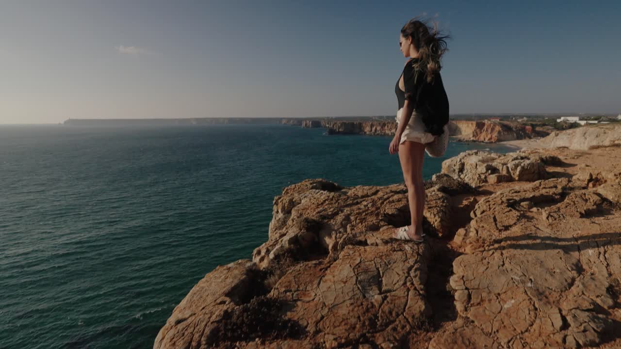 Wind blows through a woman’s hair as she gazes over the cliffs and beaches of Algarve’s stunning southern shoreline