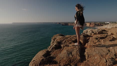 wind blows through a woman’s hair as she gazes over the cliffs and beaches of algarve’s stunning southern shoreline