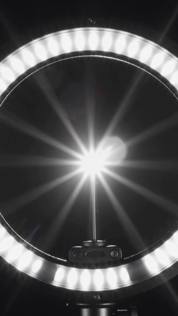 Vertical video: Recording, LED ring emitting shifting flare in dark room with central LED mount