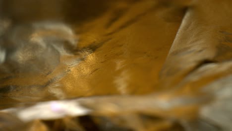 pushing towards top layer of contoured textured colorful foil with yellow and gold coloring, macro view of the foil as it moves and flows