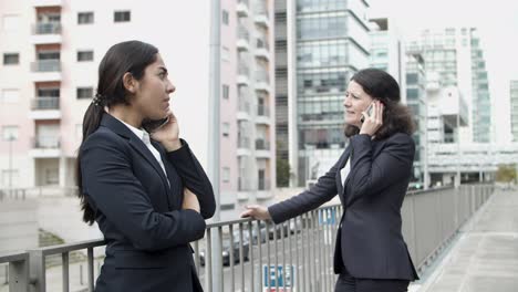 businesswomen talking by smartphones on street