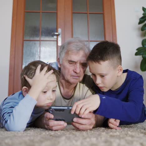 two grandchildren are teaching grandfather to play their favorite toy on the tablet in the free time of the day. modern technologies
