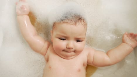 close-up of a little baby girl lying on her back in the bathroom all in foam