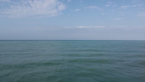 Frame-split-in-half:-Aerial-rises-above-crisp,-blue-ocean-shore-break