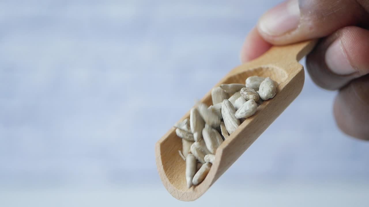 Hand pouring sunflower seeds from a wooden scoop