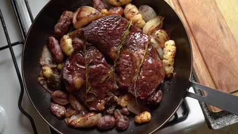 delectable roasted beef in a skillet with potatoes, onions, and rosemary leaves - close up