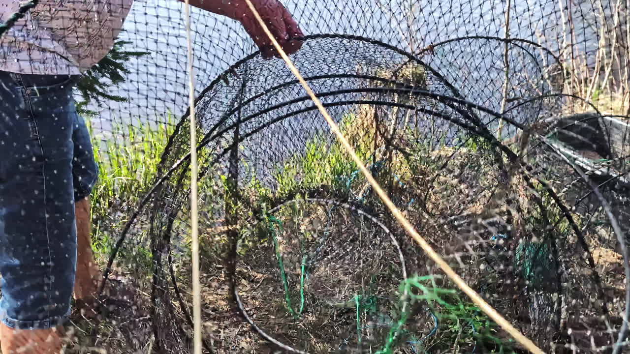 A man casts a round net into the water in a traditional fishing method, creating ripples.