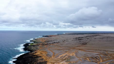 expansive volcanic coastline with rugged dirt roads leading to the ocean. waves crash against the rocky shore under an overcast sky, creating a remote, wild atmosphere.