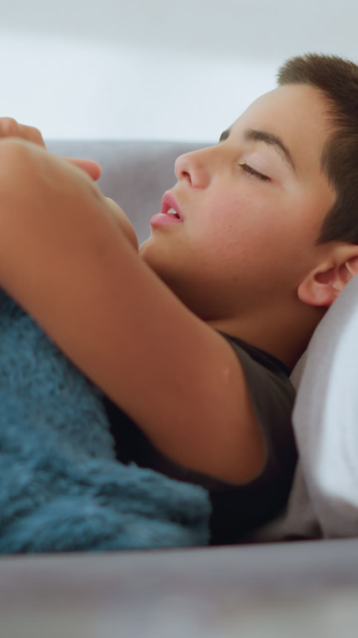 Close-up blur of glass cup with health care moment, feverish boy lying down taking thermometer to check his temperature, concerned expression, child care, health monitoring in a home setting