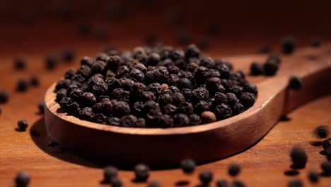 granos de pimienta de tellichería negra en una cuchara de madera en una mesa de la cocina.