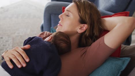 video de una madre caucásica cansada durmiendo en un sofá con un bebé recién nacido