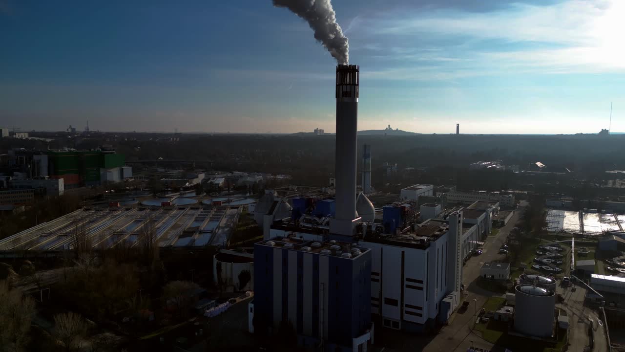 Waste to energy plant emitting smoke from its chimney, located near an urban area, environmental impact of waste. Majestic aerial view flight tilt down drone
