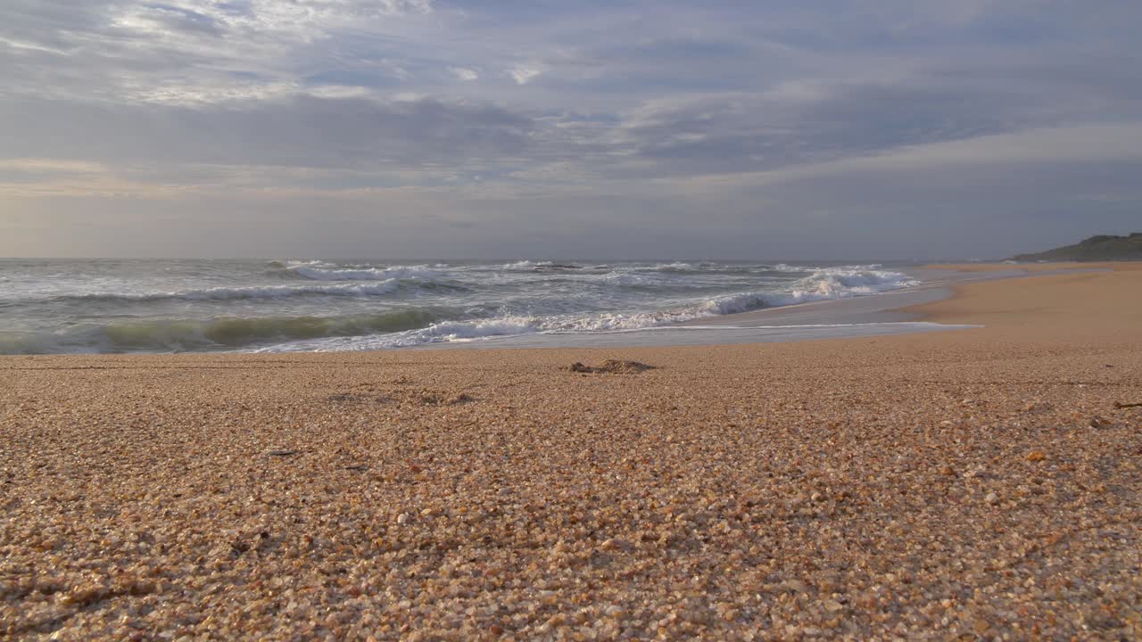 En fredfyldt kystscene udfolder sig med bølgernes rytmiske bevægelse, der skyller ind på en stor sandflade under en himmel fyldt med bløde skyer ved Ramsgate, Sydkysten, KwaZulu-Natal.