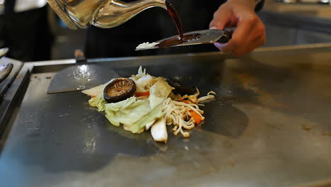 close-up of a skilled chef preparing teppanyaki japanese cuisine on a hot iron griddle in front of guests, grilling fresh ingredients with flair. perfect for japanese food culture and live cooking