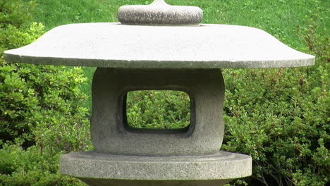 close-up of a japanese snow lantern with azalea bushes in background