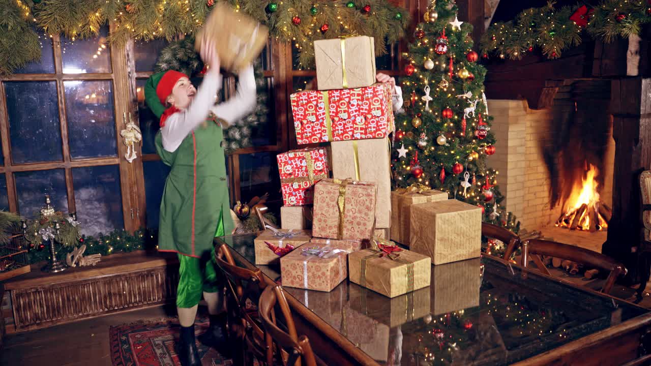 Two elves are standing in specially decorated room near the table, holding presents in hands. Feast fireplace in the background. Christmas spirit concept close up video. Christmas eve. New Year is coming. Elves are putting presents on the table. Presents are falling down from the table.
