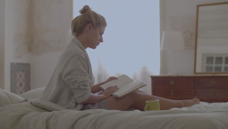 focused woman sitting on bed and reading book after waking up