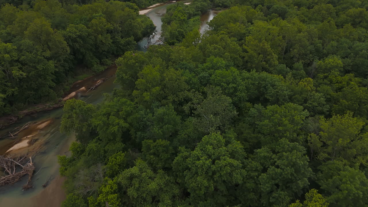 Winding forest river flows gently as boat races leaving wake between forested green hills, Lake Eucha, Tagg flats riverine region, aerial