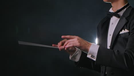 concert of classical music under direction of an orchestra conductor. man waves his baton to synchronize and conducting musicians in theater. black background with smoke and backlight. close up