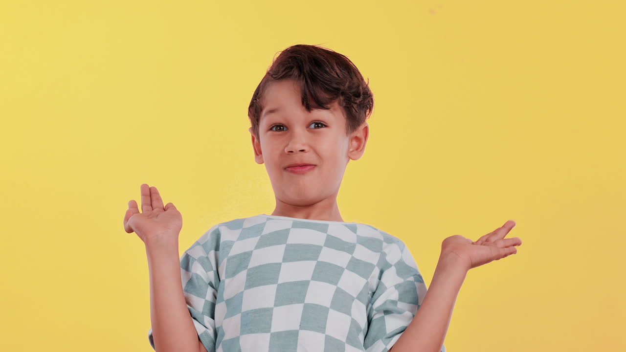 Young boy shrugging on yellow background
