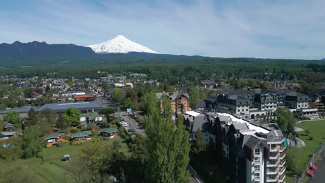 descending drone view of pucón with iconic villarica volcano in the background and urban architecture framed by trees and mountain scenery