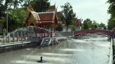 Water-fountains-releasing-and-spouting-water-into-the-canal-of-a-temple-complex-in-Bangkok,-Thailand